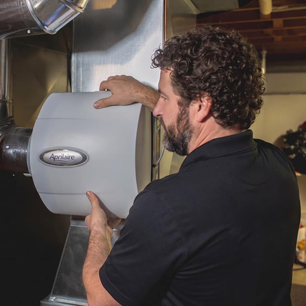HVAC technician inspecting Aprilaire whole-home humidifier installed on ductwork