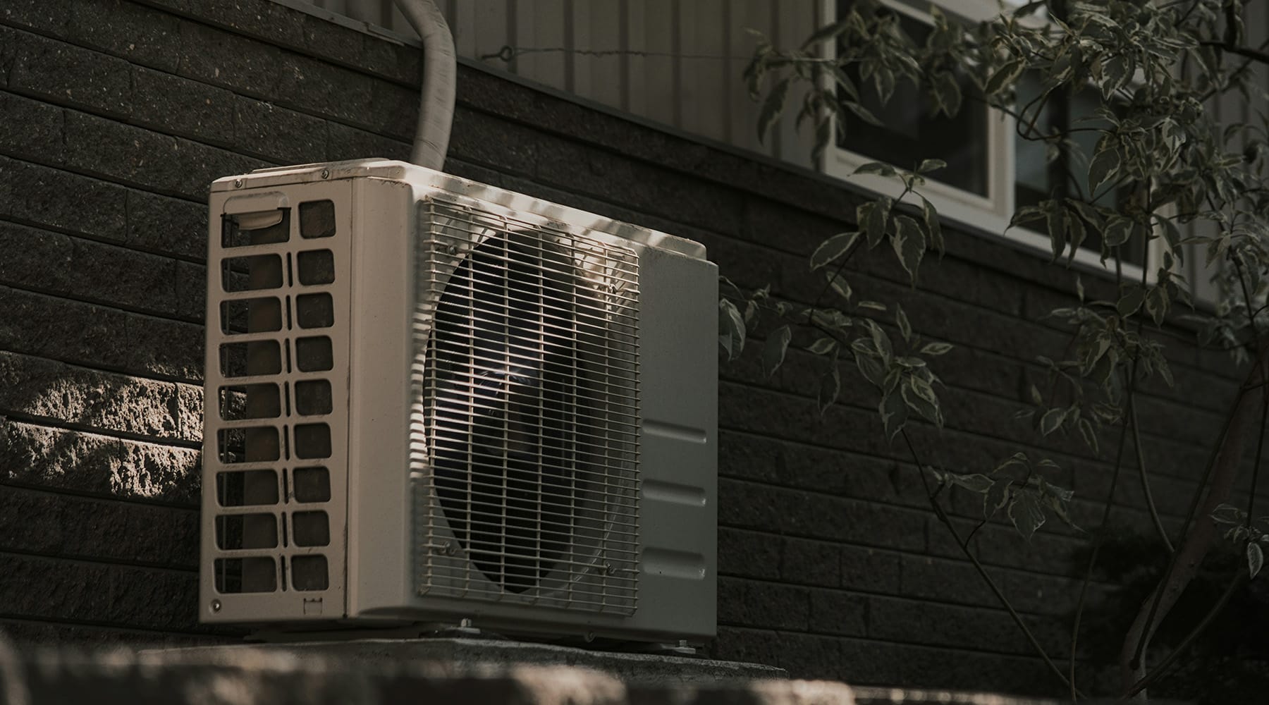 Mini split heat pump condenser unit mounted on dark brick wall exterior