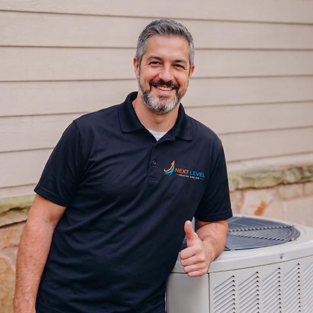 Next Level Heating and Air technician giving thumbs up beside condenser unit