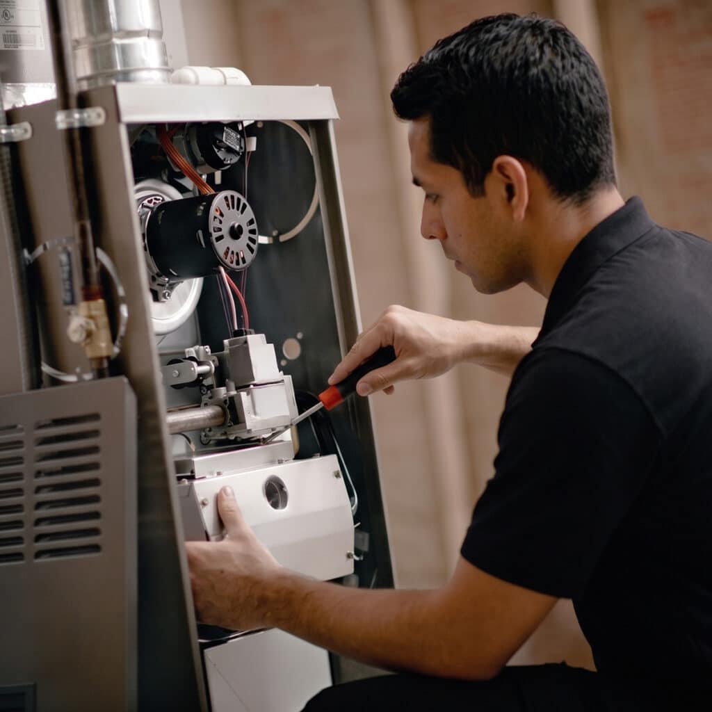 HVAC technician using screwdriver to repair gas furnace burner assembly