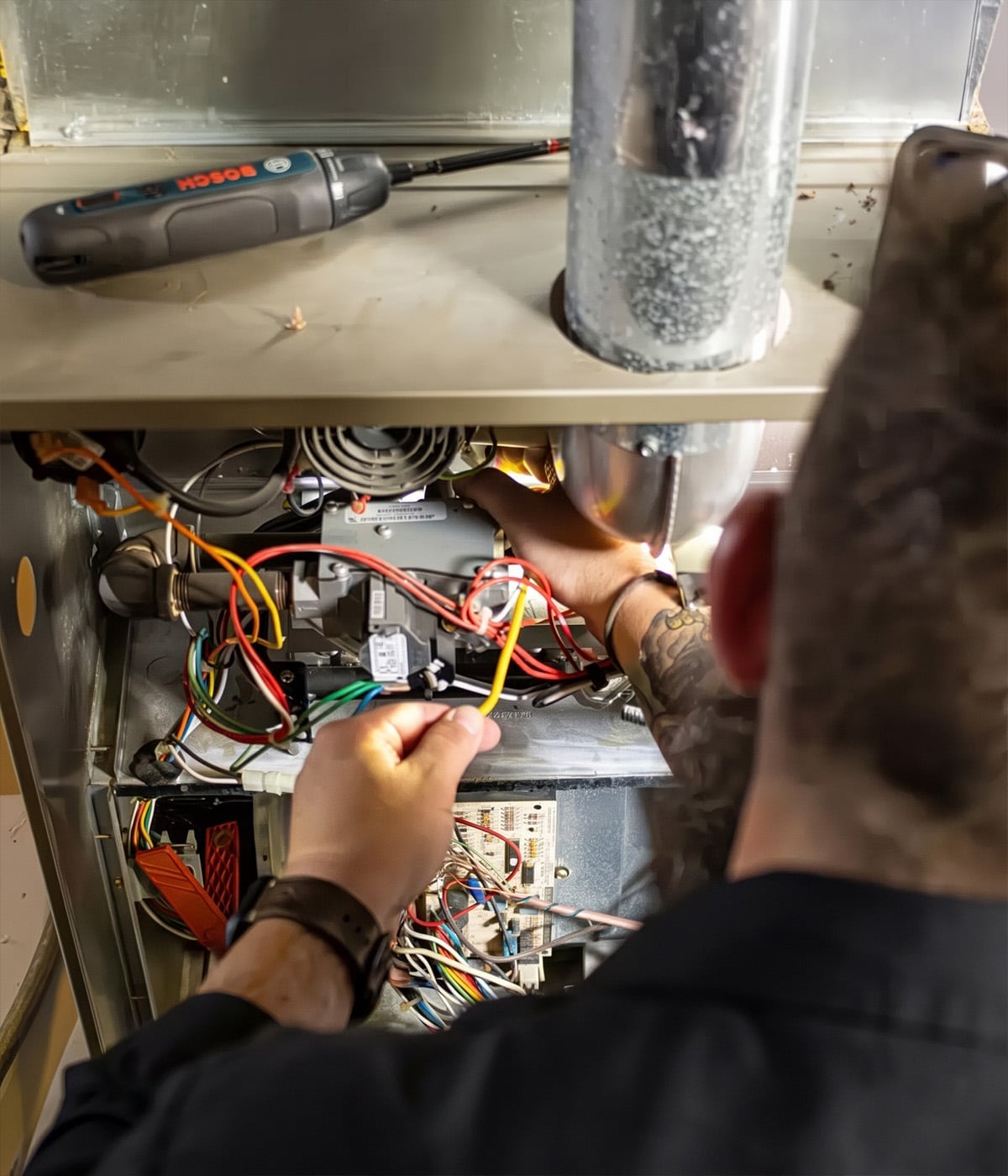 Over-the-shoulder view of a Next Level Heating & Air tech tracing wires at a furnace gas valve on a Richmond, KY service call.